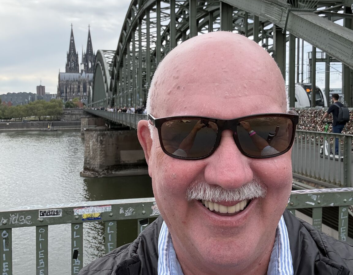 Hank Howie smiling on Cologne’s Hohenzollern Bridge with Cologne Cathedral behind him during Gamescom 2026