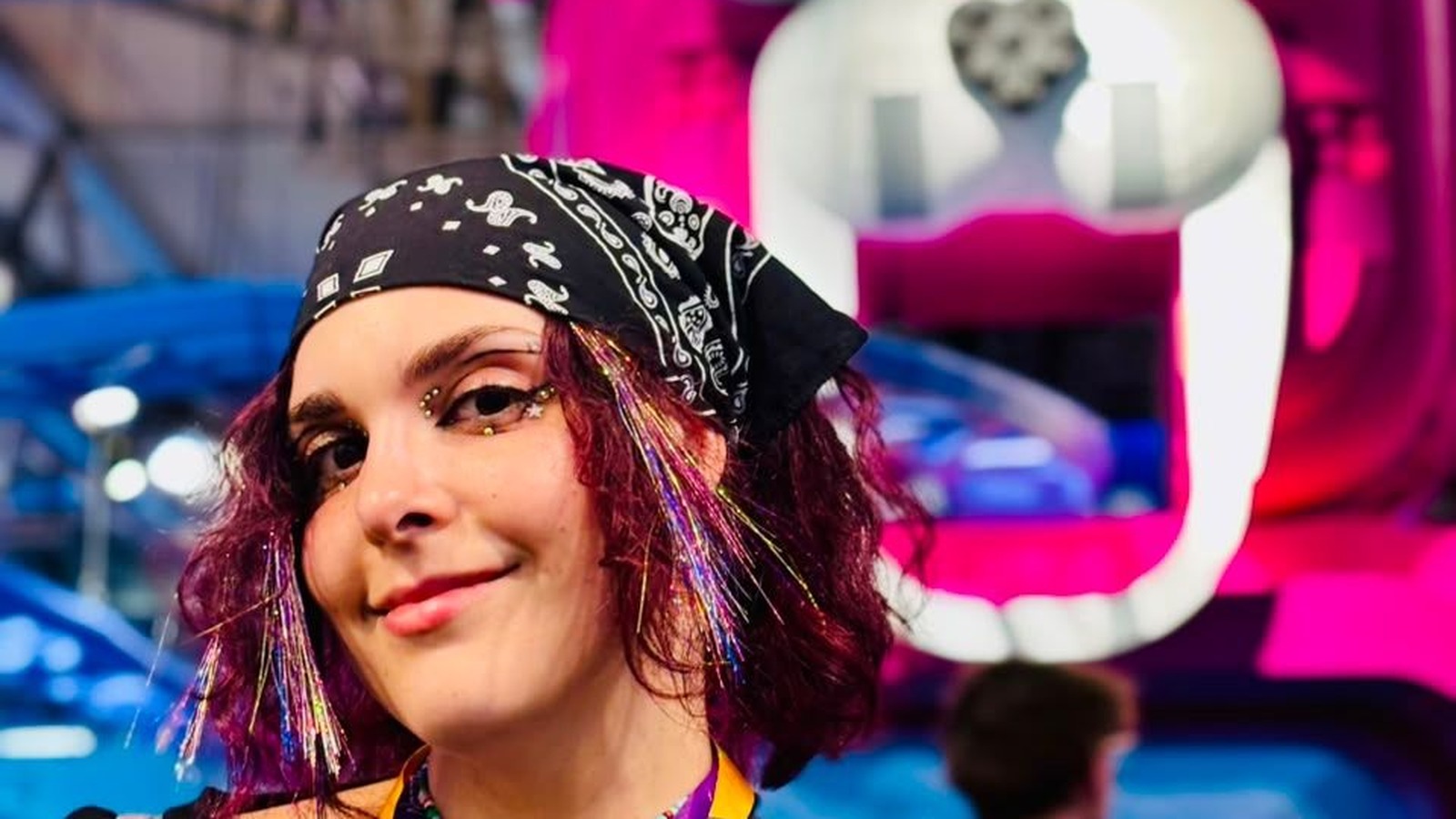 Ruslana Kruchek at Gamescom 2026, wearing a black bandana with a bright pink creature display behind her